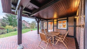 An outdoor patio with a brick floor, wooden tables and chairs, and a brick wall with windows. - "Havelquelle" Vacation Home in Kratzeburg, surrounded by beech forests and lakes (Kratzeburg)