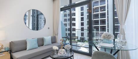 A modern living room with a sofa, a round glass coffee table, and a dining area with a glass table and chairs.