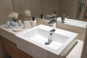 Une salle de bain moderne avec un lavabo blanc, un miroir et des articles de toilette posés sur le comptoir.