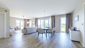 A spacious living area with a dining table, chairs, a sofa, and a kitchen area.