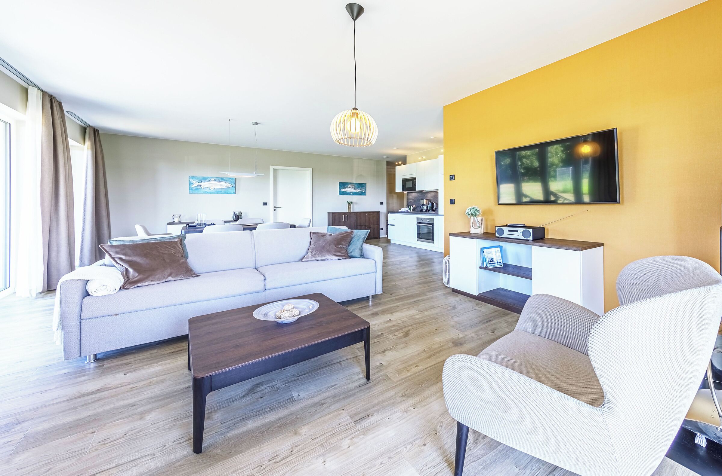 A modern living room with a sofa, coffee table, and armchair, a kitchen in the background, and a dining area.