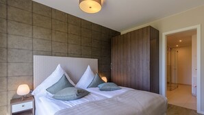 A modern bedroom with a large bed, a nightstand, a wardrobe, and a walk-in closet.