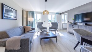 A modern living room with a sofa, two armchairs, a coffee table, and a TV. - 5 star apartment Strandräuber with sea view in Wustrow (Wustrow)