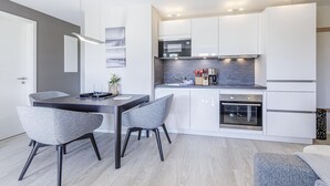 A modern kitchen with white cabinets, a built-in oven, and a dining area with two grey chairs. - 5 star apartment Strandräuber with sea view in Wustrow (Wustrow)