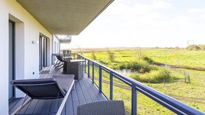 A balcony with outdoor furniture, a view of a green field, and a wind turbine in the distance.
