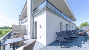 A modern outdoor deck with wicker furniture and sun loungers, overlooking a green landscape.