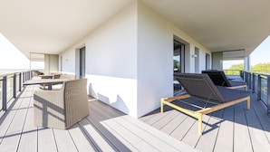 Terraço com duas espreguiçadeiras e uma mesa, com vista para a água.