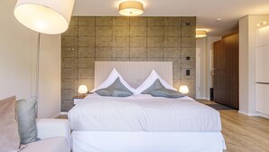 A modern hotel room with a large bed, bedside lamps, a headboard with a geometric pattern, and a wooden wardrobe.