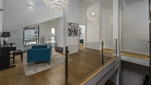 Ein geräumiger Wohnbereich mit einem blauen Sofa, einer Glasreling und einer modernen Kronleuchter.