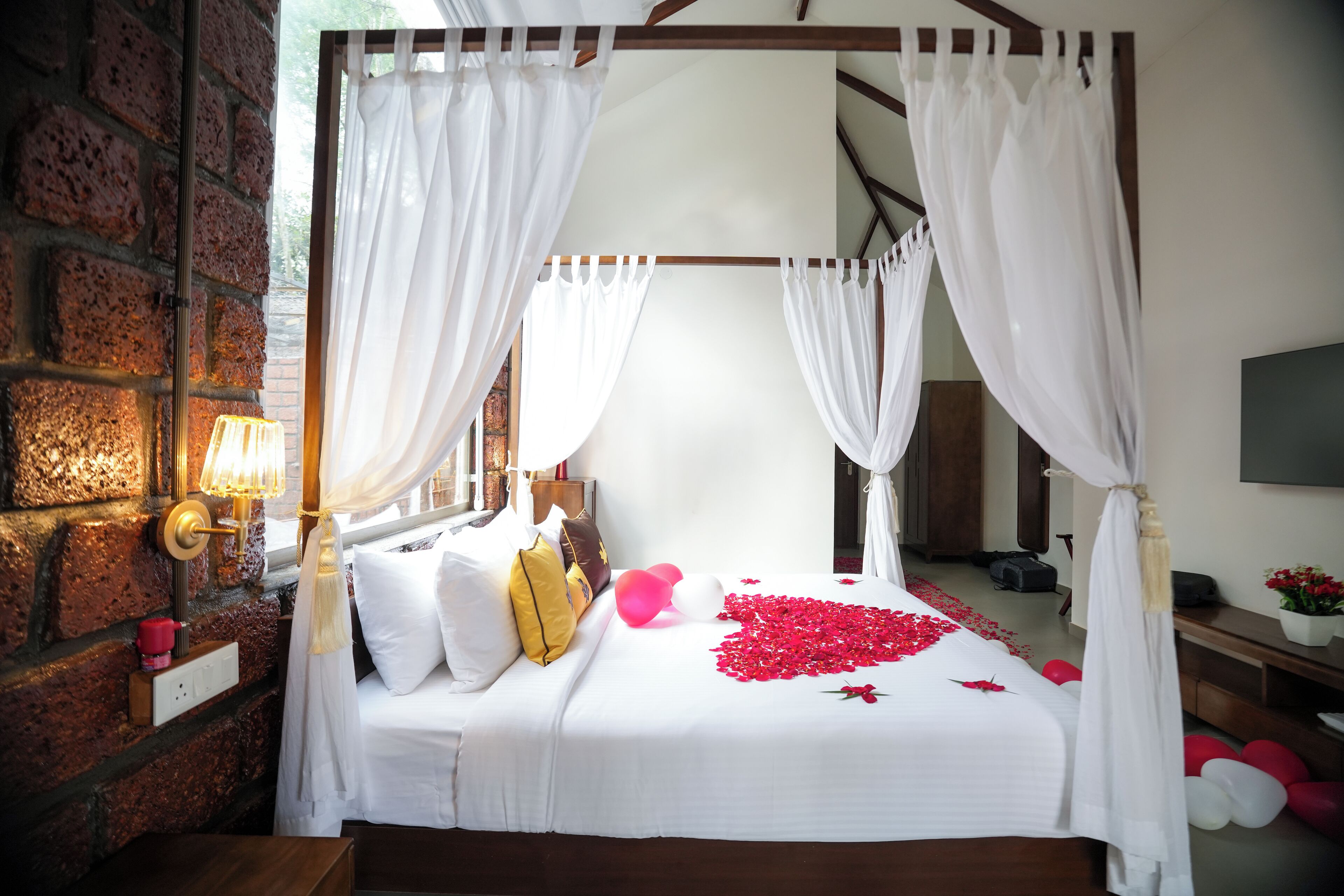 A four-poster canopy bed with white linens, a brick wall, and a bedside lamp.