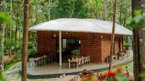 A brick building with a covered patio area, surrounded by trees. - TGI Redolent Resort & Spa (Somvarpet)