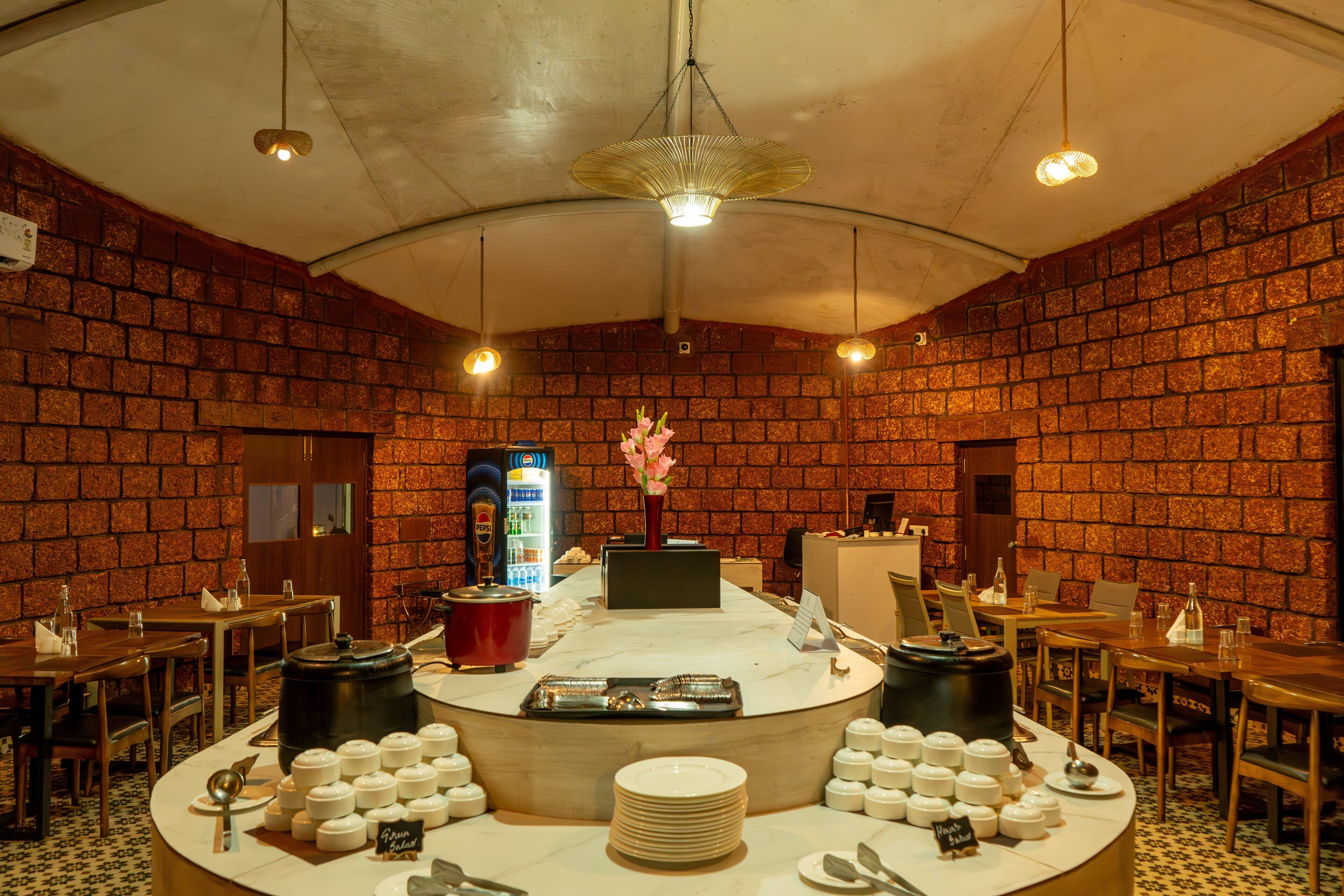 Un restaurante con paredes de ladrillo, una barra central con productos alimenticios y mesas con sillas.