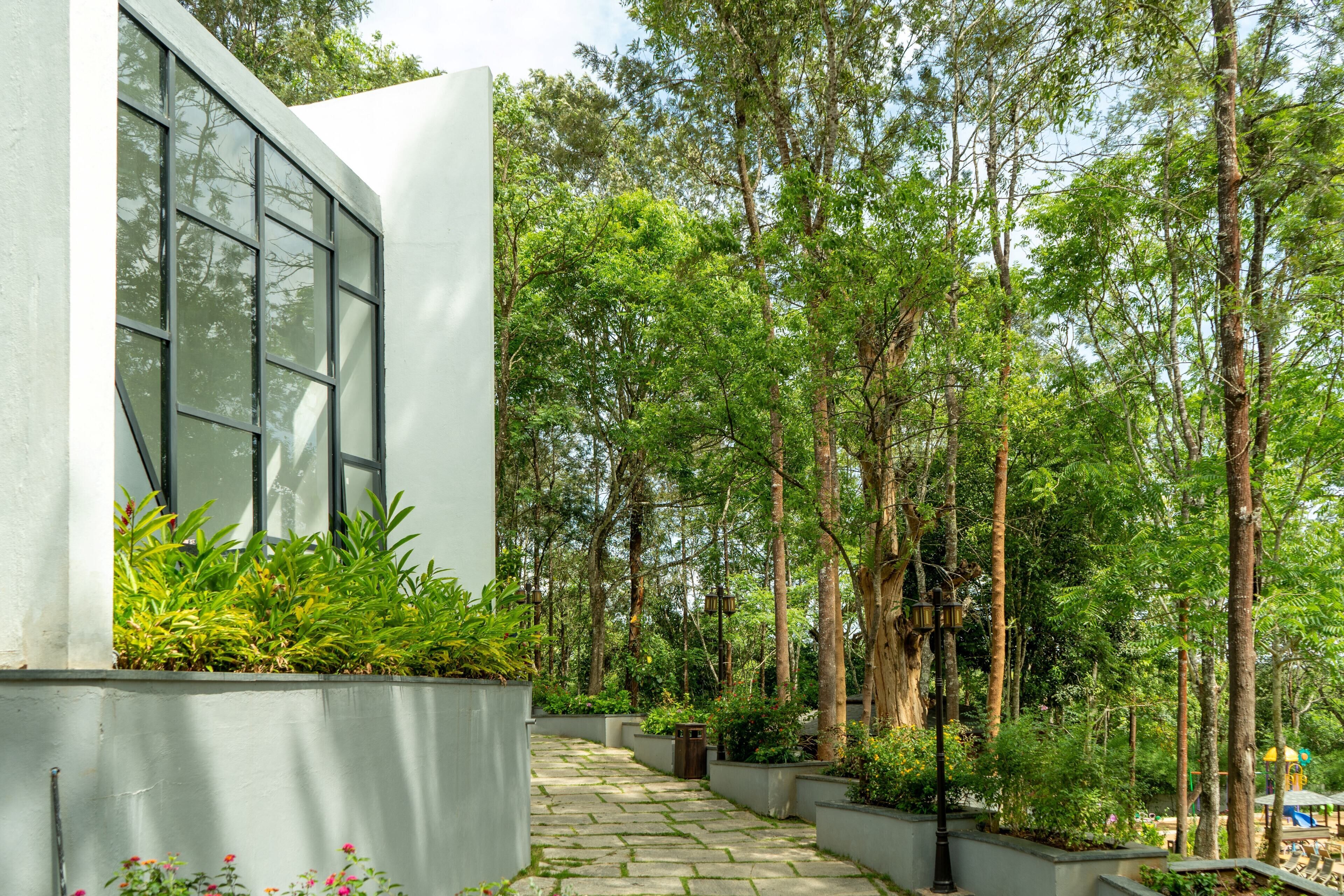 Un edificio moderno con amplios ventanales, rodeado de un exuberante jardín con árboles altos y un sendero de piedra.