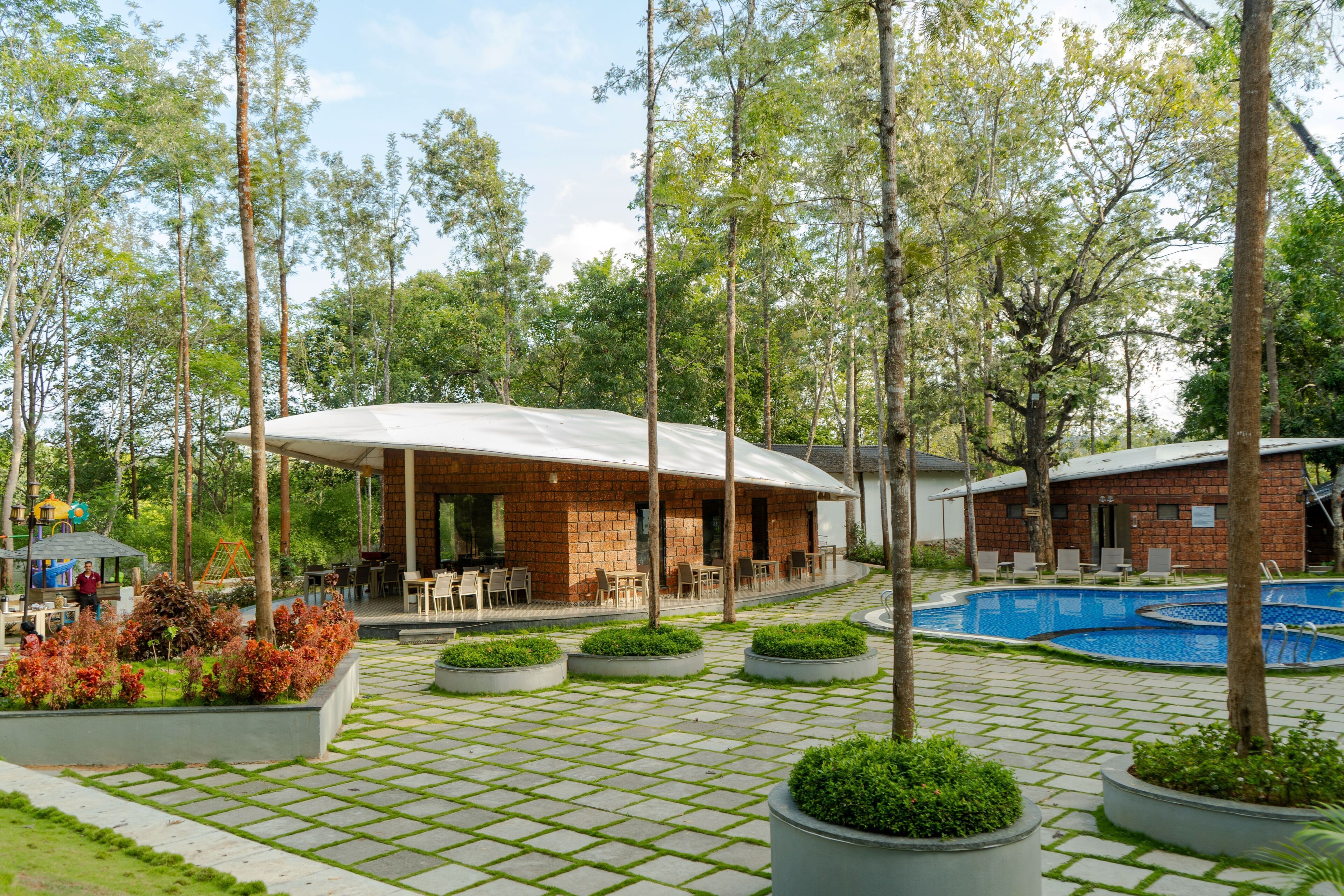 Un edificio con un porche cubierto, piscina y jardín con jardineras.