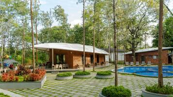 Un edificio con un porche cubierto, piscina y jardín con jardineras.