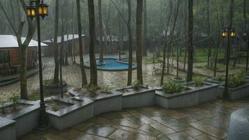 A courtyard with a pool, surrounded by trees and stone planters, under rainy weather.