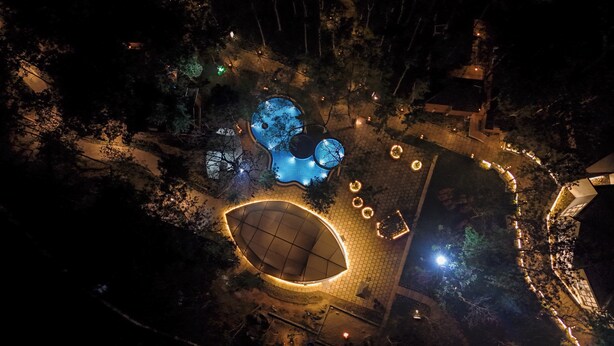 An aerial view of a park with illuminated structures, pathways, and a large circular area with a dome-like roof. - TGI Redolent Resort & Spa (Somvarpet)