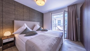 Ein modernes Hotelzimmer mit einem großen Bett, einem Nachttisch, einer Wandleuchte und Blick auf die Stadt durch große Fenster.