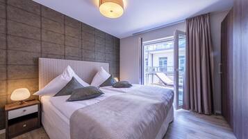 Ein modernes Hotelzimmer mit einem großen Bett, einem Nachttisch, einer Wandleuchte und Blick auf die Stadt durch große Fenster.