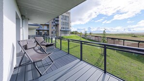 Un balcon avec deux fauteuils de jardin et une vue sur une zone verdoyante et des bâtiments en arrière-plan.