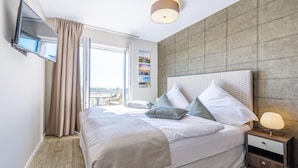 Ett modernt hotellrum med en stor säng, en platt-TV som är monterad på väggen, ett nattduksbord med en lampa och utsikt över staden genom fönstret.