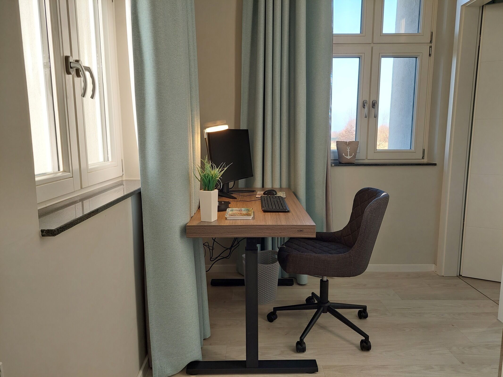 A workspace with a desk, chair, computer, and a window with curtains.
