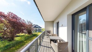 Varanda com mesa e cadeiras, vista para um jardim e um edifício.