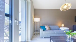 Uma sala de estar moderna com um sofá cinzento, um candeeiro de chão e uma mesa com um vaso de flores.