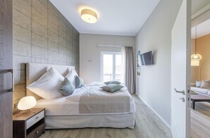 Ein modernes Schlafzimmer mit einem großen Bett, einem Nachttisch mit Lampe, einem an der Wand montierten Fernseher und einem Fenster mit Vorhängen.