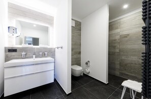 Ein modernes Badezimmer mit einem weißen Waschtisch, einem großen Spiegel und einer Duschkabine mit dunklem Boden.
