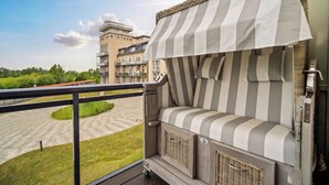 Un balcón con un toldo a rayas, una silla de mimbre y vistas a un edificio y follaje.