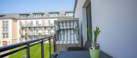 A balcony with a view of a building, a small table, and a potted plant.