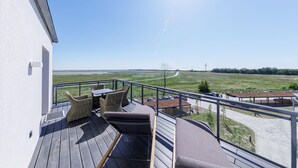 A balcony with wicker furniture, a view of a rural landscape, and a clear sky. - 5-star Boddenidylle vacation apartment with balcony and view of the Bodden and Baltic Sea (Wustrow)