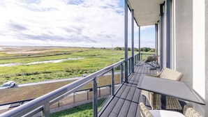 A balcony with wicker furniture, a view of a green landscape, and a wind turbine in the distance. - 5-star vacation apartment Ostseepanorama with beach chair, between Baltic Sea & Bodden (Wustrow)