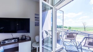 Un salon moderne doté d’un téléviseur à écran plat, d’une petite table et d’une porte vitrée donnant sur une terrasse extérieure avec des chaises.