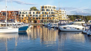 Un puerto deportivo con varias embarcaciones amarradas, un edificio de varios pisos con balcones, y un cielo despejado.