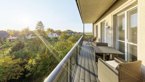 A balcony with a table and chairs, overlooking a lush garden and houses. - Boddendomizil vacation apartment with balcony and beach chair in Wustrow (Wustrow)