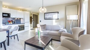 A modern living room with a sofa, coffee table, and dining area. There is a kitchen in the background with a microwave and cabinets. - Boddendomizil vacation apartment with balcony and beach chair in Wustrow (Wustrow)