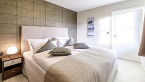 A neatly arranged bedroom with a large bed, a bedside table with a lamp, and a door to the right. - Boddendomizil vacation apartment with balcony and beach chair in Wustrow (Wustrow)