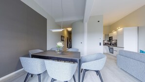 Un espace repas moderne avec une table en bois foncé et des chaises à revêtement gris, un canapé gris et une cuisine en arrière-plan.