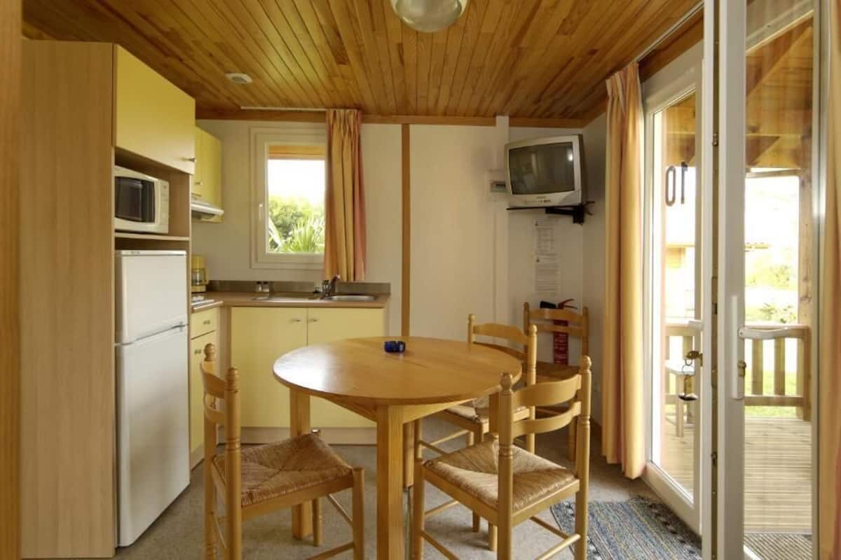 Una cucina compatta con un tavolo da pranzo e sedie, un forno a microonde, un frigorifero e una televisione appesa al muro.