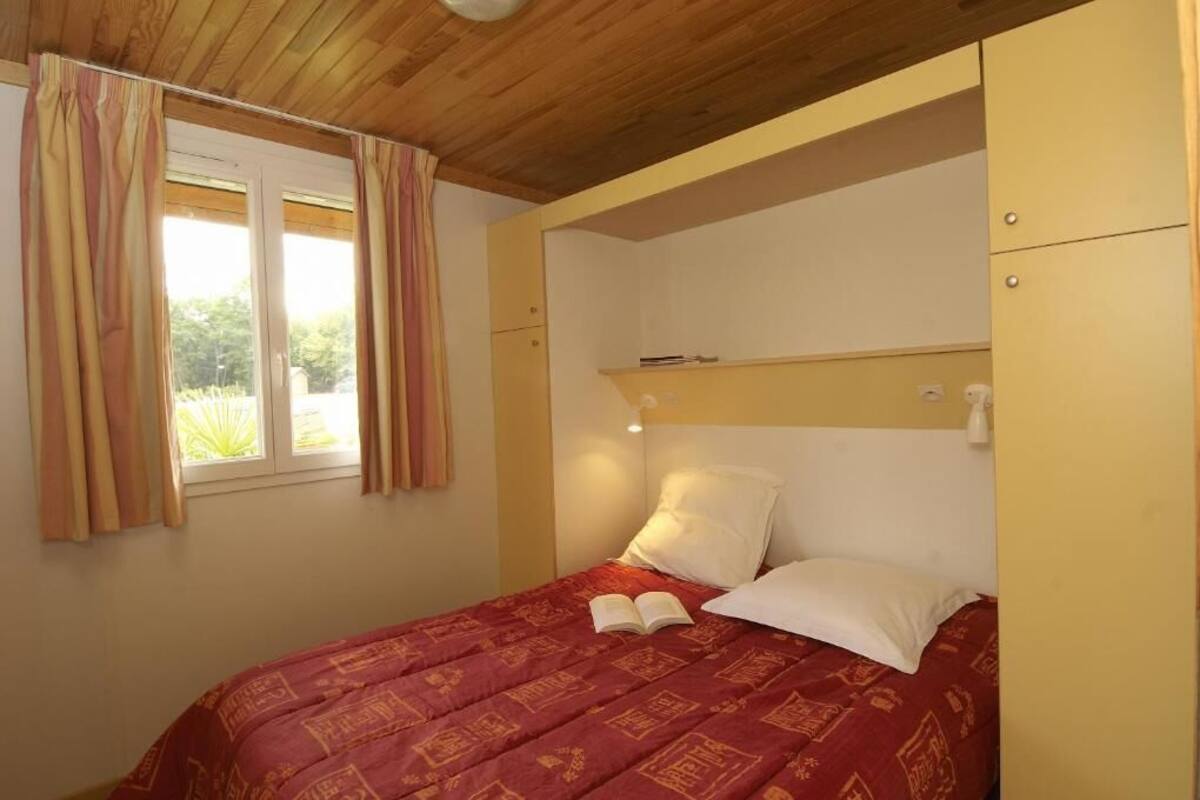 Una camera da letto con un letto, una finestra con tende, un comodino con una lampada e un armadio.