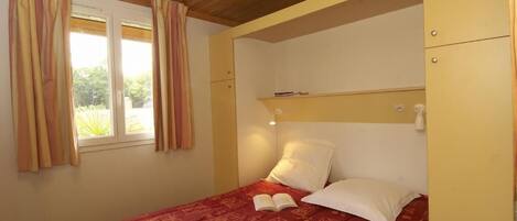 Un dormitorio con cama, ventana con cortinas, mesita de noche con lámpara y armario.