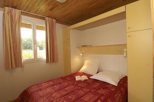 Quarto com cama, janela com cortinas, mesa de cabeceira com abajur e guarda-roupa.
