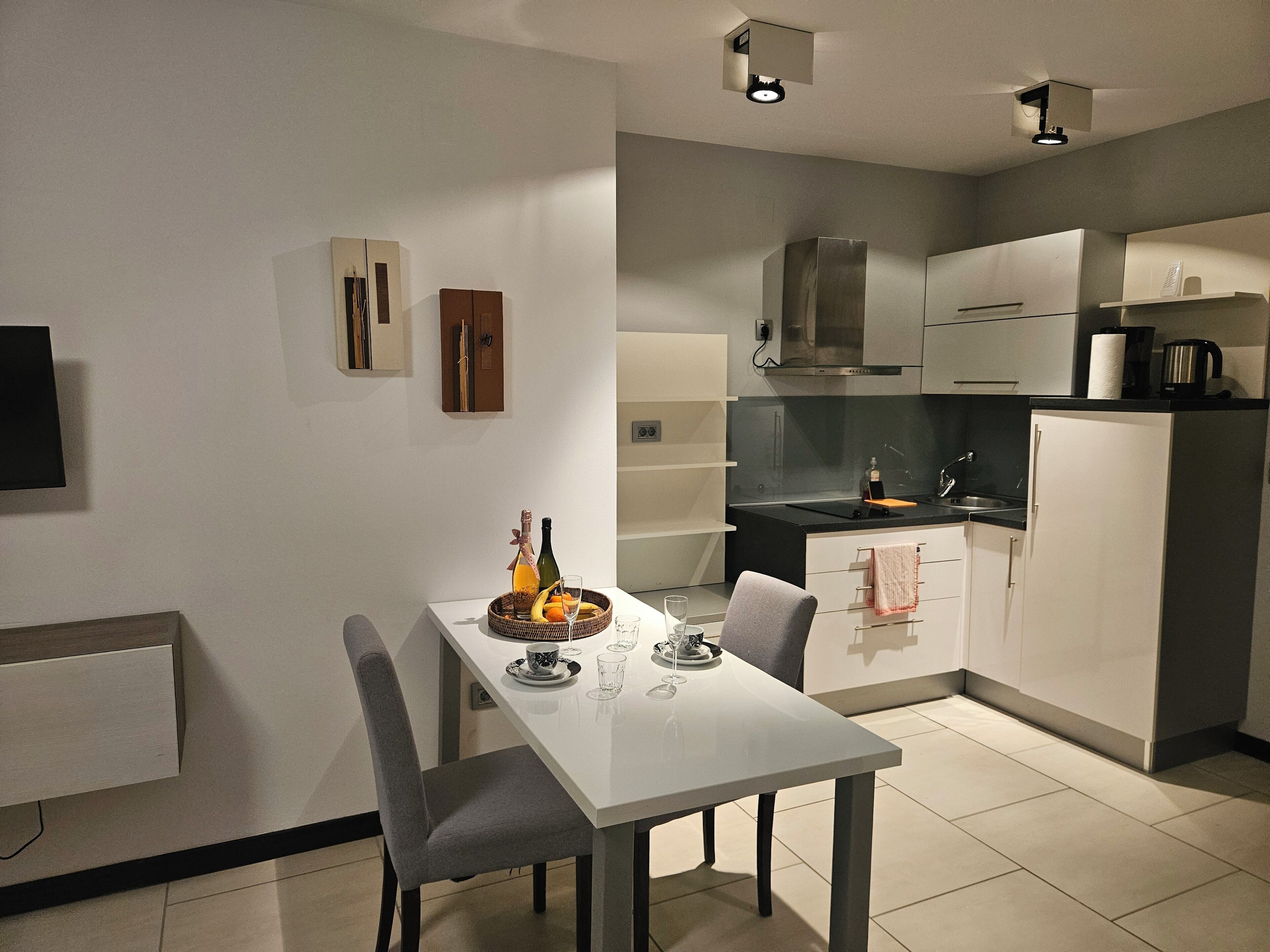 A modern kitchen with a dining table set for two, a built-in oven, and a coffee maker.