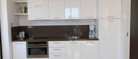 Eine moderne Küche mit weißen Schränken, einem eingebauten Backofen, einer Kaffeemaschine und einer Spüle aus Edelstahl.