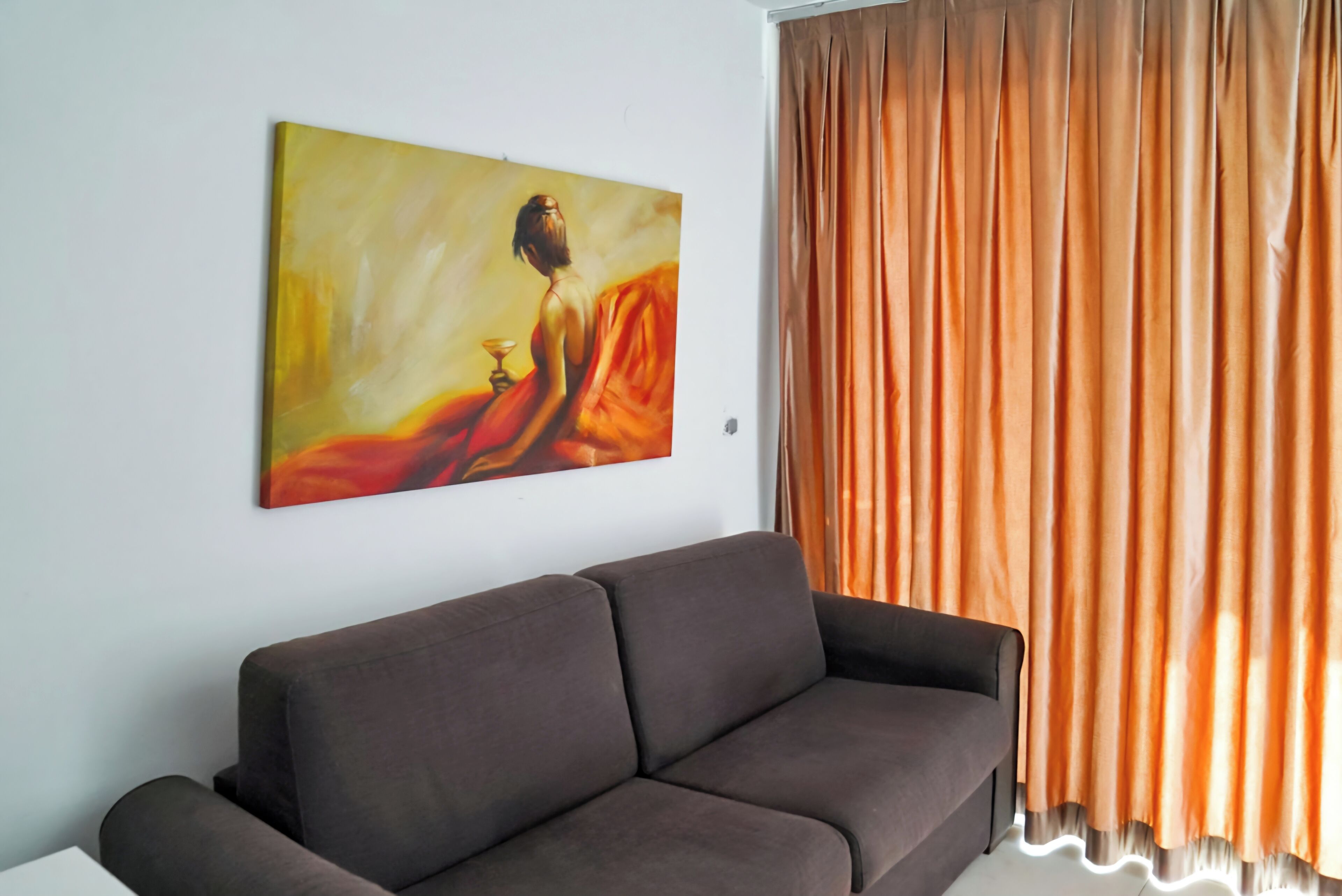 Un salon moderne avec un canapé marron foncé, un tableau accroché au mur et des rideaux orange.
