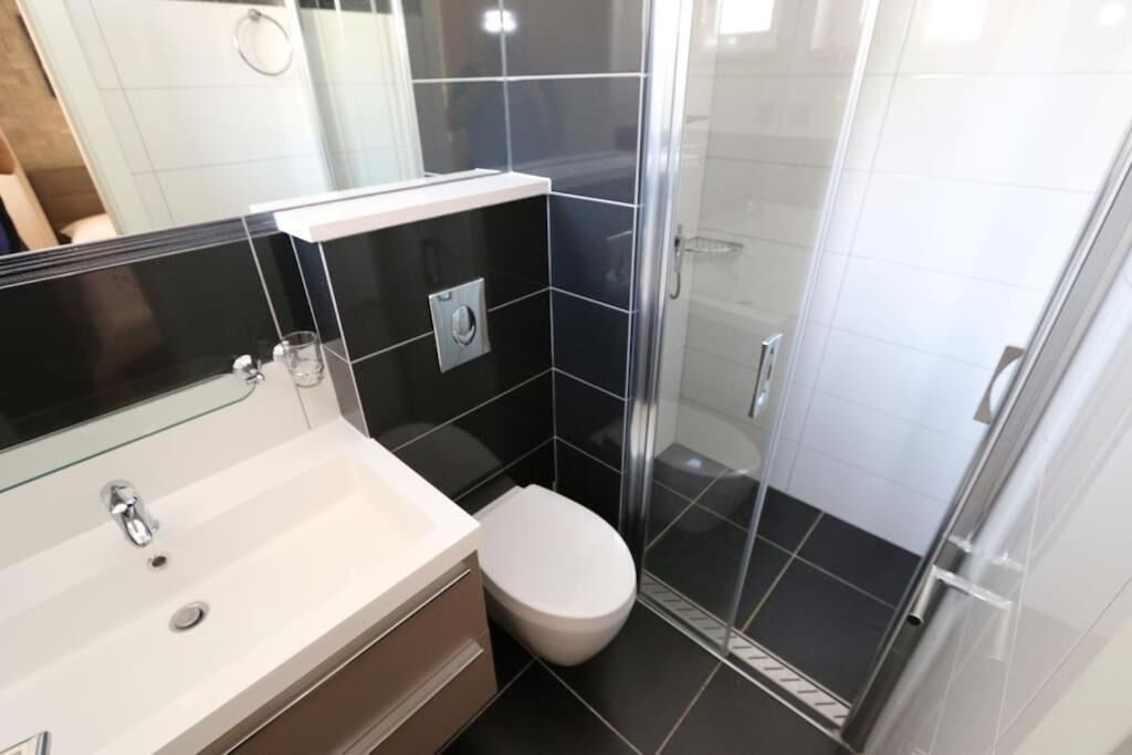 Un baño moderno con un lavamanos blanco, un inodoro y una cabina de ducha de vidrio.