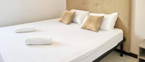 A neatly made bed with white linens and two beige pillows, a wooden headboard, and a small bedside table.