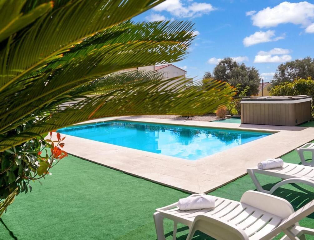 Una piscina con agua azul cristalina, rodeada de césped artificial verde y sillas de descanso blancas.